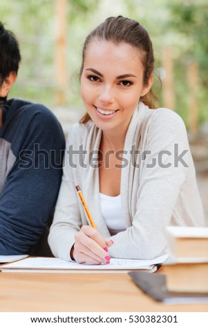 Smiling attractive young woman sitting and writing at the table