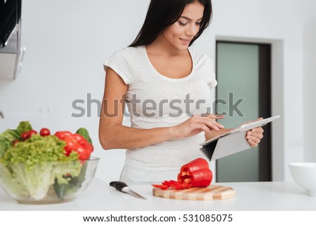Picture of young pretty woman reading recipe from tablet computer in the kitchen. Looking at tablet computer.