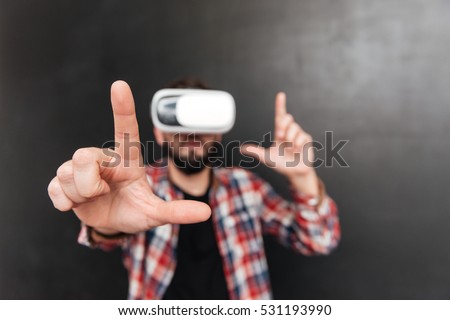 Man dressed in shirt in a cage and wearing virtual reality device standing over chalkboard. Focus on hands.