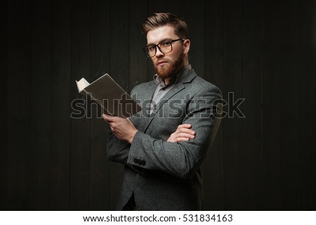 Portrait of a smart young man in casual suit standing and holding book isolated on the black wooden background