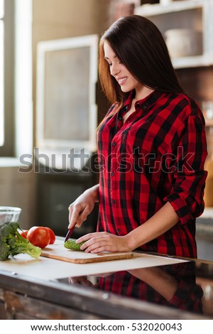 Vertical image of smiling cute woman in red shirt cooking in kitchen. Side view