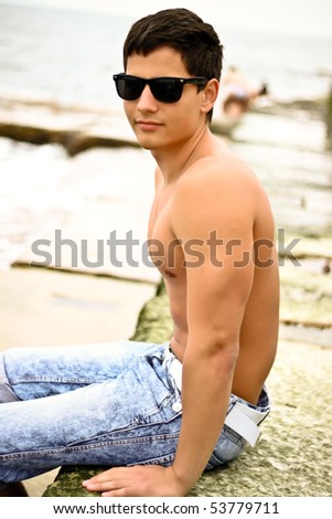 stock photo Young sexy man in sunglasses sitting on the beach