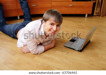 Young smiling man lying on the floor with laptop at home looking at the camera