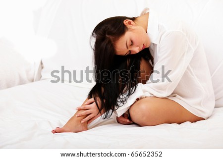 Beautiful young woman sitting on a bed and touching her legs