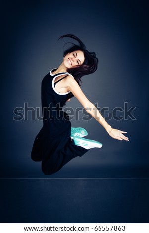 Young dancing woman in black suit on dark background