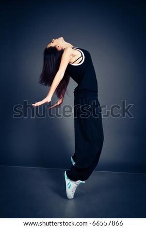 Young dancing woman in black suit on dark background