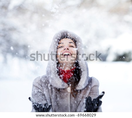 Cute young woman playing with snow in fur coat outdoors