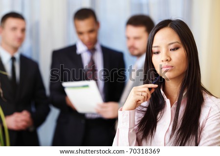 Portrait of young pensive asian woman with her business partners on the background