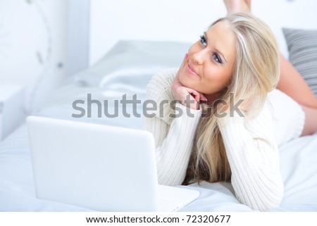 Young beautiful happy woman lying on the bed with laptop