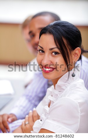 Smiling latin business woman looking at camera with satisfaction and working colleagues in office
