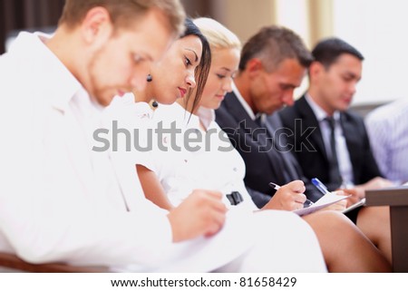 Business people sitting in a row at meeting and making notes. Focus on woman