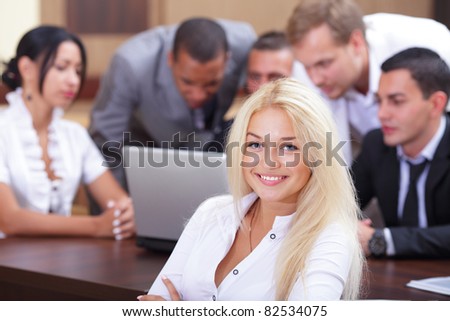 Portrait of a young laughing woman with her colleagues working behind