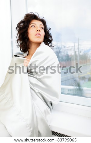 Beautiful woman wrapped in blanket standing at the window and waiting