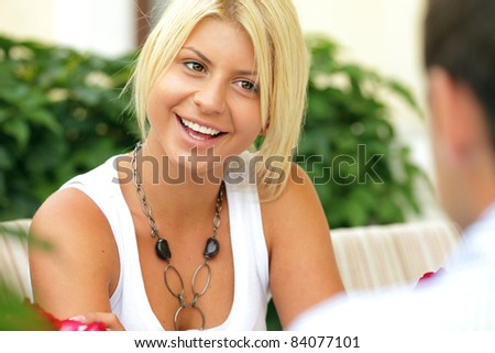 Beautiful young woman outdoors sitting at the table and flirting with the man in front