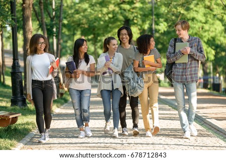 Image of multiethnic group of happy young students walking outdoors. Looking aside.