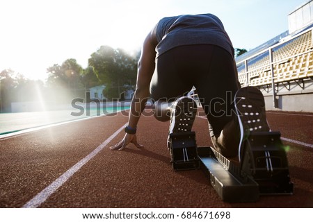 Back view of a young man in starting position for running on sports track