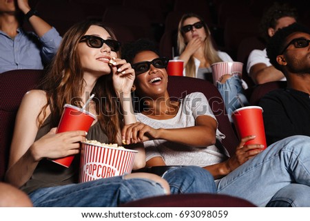 Picture of cheerful friends sitting in cinema watch film eating popcorn and drinking aerated sweet water.