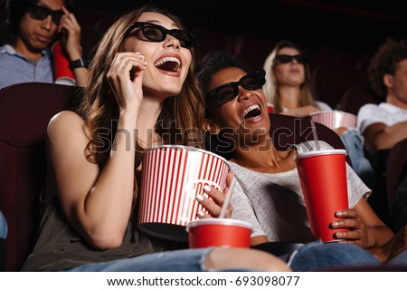Picture of cheerful friends sitting in cinema watch film eating popcorn and drinking aerated sweet water.