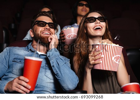 Image of happy friends sitting in cinema watch film eating popcorn and drinking aerated sweet water.