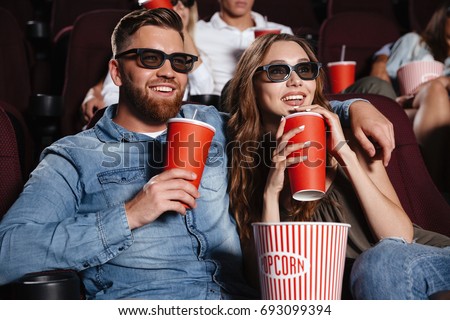 Picture of concentrated loving couple friends sitting in cinema watch film eating popcorn and drinking aerated sweet water.