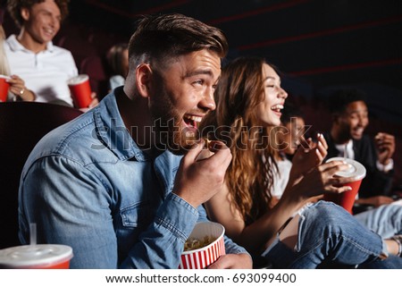Image of laughing friends sitting in cinema watch film eating popcorn and drinking aerated sweet water.