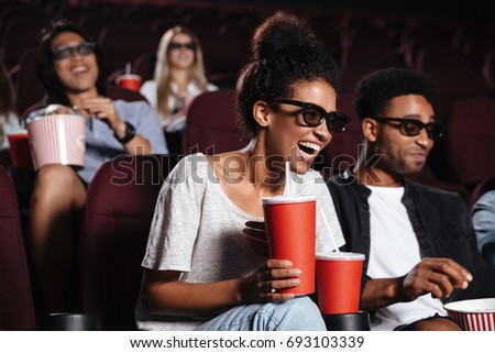 Picture of happy young friends sitting in cinema watch film drinking aerated sweet water.