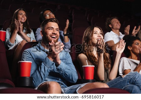 Happy smiling audience clapping hands while sitting at the cinema and watching movie
