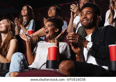 Multiethnic happy audience clapping hands while sitting at the cinema and watching movie