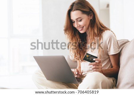 Young confident pretty woman working with laptop and credit card at home