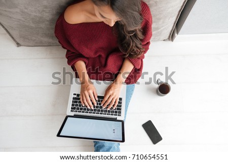 Top view of a young woman holding laptop computer on her lap while sitting at home