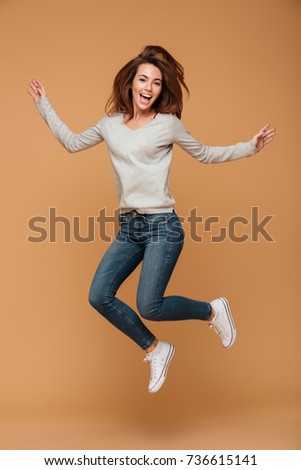 Full length photo of charming young woman in casual wear jumping over beige background