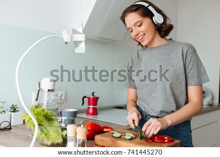 Portrait of a smiling attractive woman listening to music with headphones while cooking at the kitchen