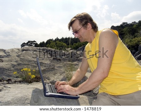The man works on a portable computer in mountains on a background of the blue sky