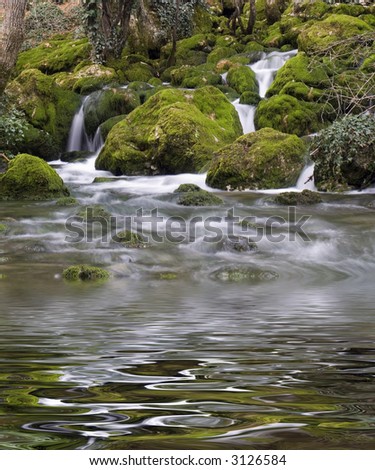 Falls on the mountain river with boulders the overgrown with a moss