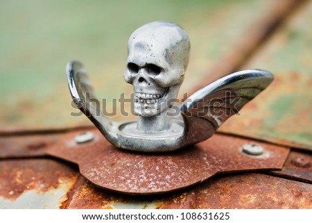 Chrome skull with wings Hood Ornament on a rusty car