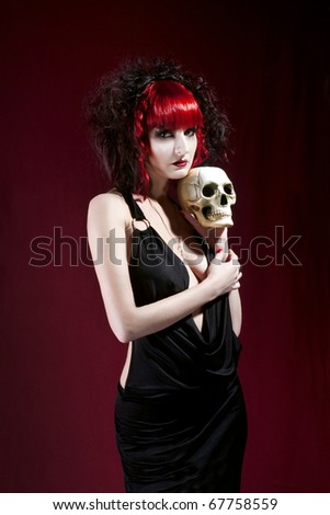 Studio portrait of young pale woman in black dress holding skull