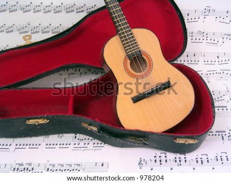 Acoustic guitar in open guitar case with sheet music background.