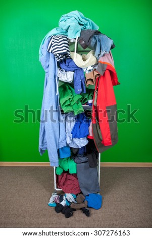 Messy winter clothes thrown on a shelf. Untidy cluttered wardrobe with colorful clothes and accessories against the wall