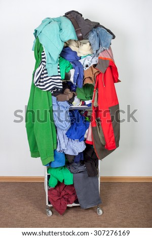 Messy winter clothes thrown on a shelf. Untidy cluttered wardrobe with colorful clothes and accessories against the wall