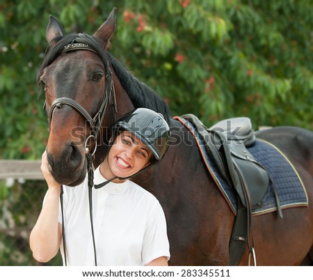 Cheerful young jockey woman  with purebred horse outdoors