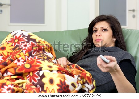 Bored young woman holding remote-control and watching tv at home