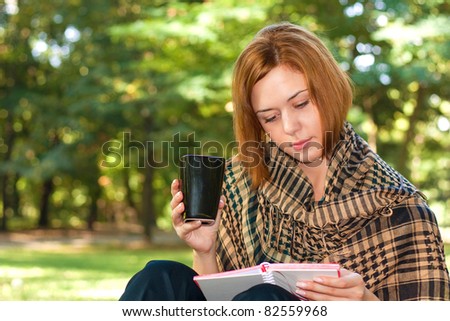 Ginger-haired woman sitting on a bench,drinking coffee and reading book
