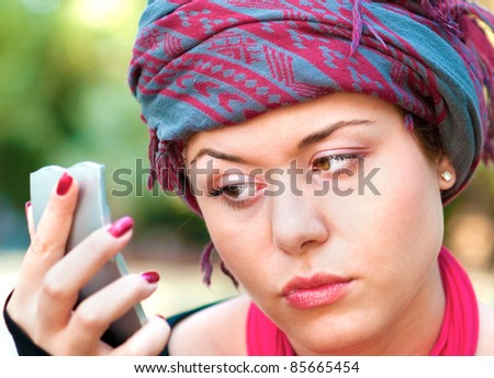 Portrait of healthy young woman wearing colorful scarf and looking in a mirror for wrinkles