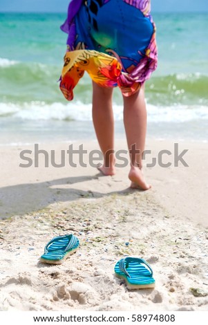 Flip-flops on beach and woman\'s leg going to the sea. Focus on flip-flops