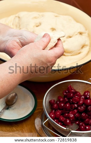 Female hands making small pies with cherry on a table