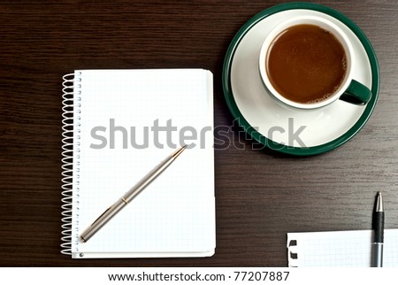 Notebook, silver pen and cup of coffee on dark desk