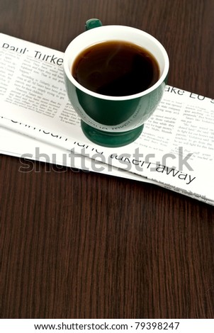 Hot cup of coffee and newspaper on dark desk