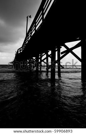 A black and white image of a fishing pier going off into the distance