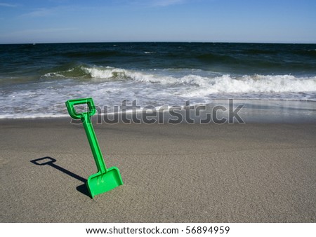 Beach toy shovel in the sand, with ocean waves on the background.