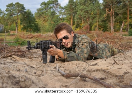 Teenager, boy lying in his battle dress, sunglasses and a rifle, Air Soft Gun